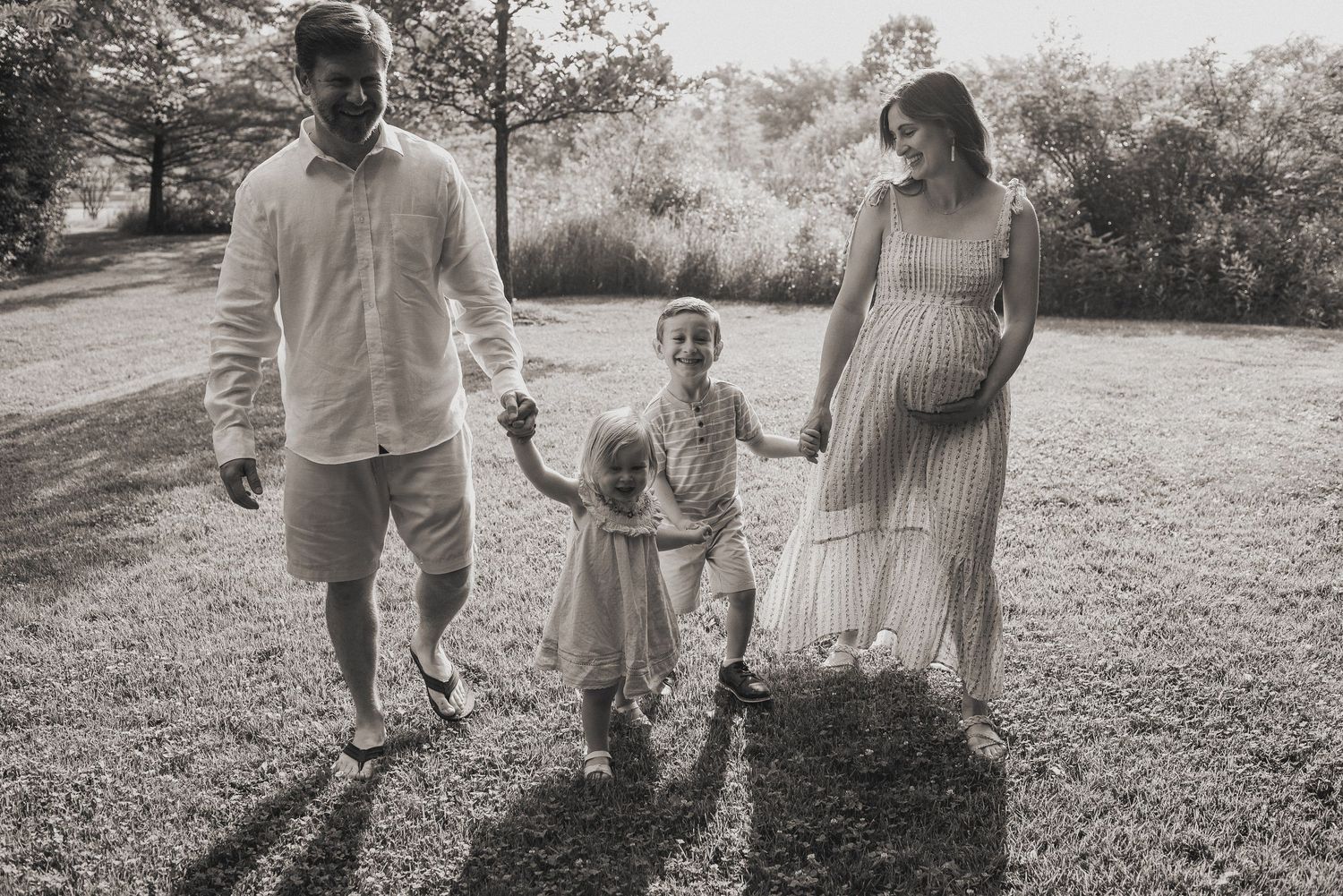 Black and white family portrait showing three figures walking together in a sunny outdoor setting.