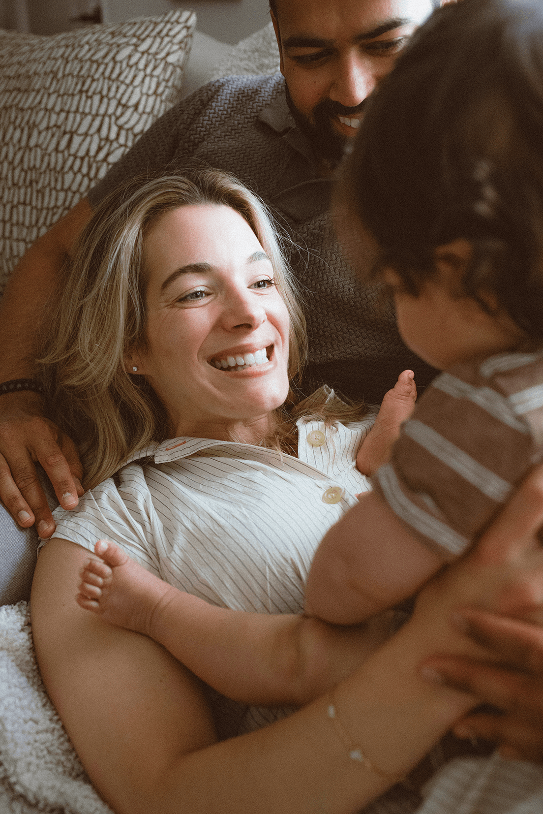 A series of candid images showing intimate bonding moments between parent and young child on a bed with gray bedding.