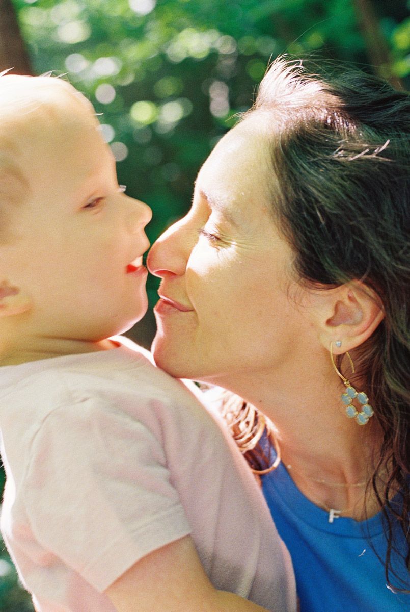 Woman with dark hair sharing a tender nose-to-nose moment with a baby in a pink shirt outdoors.