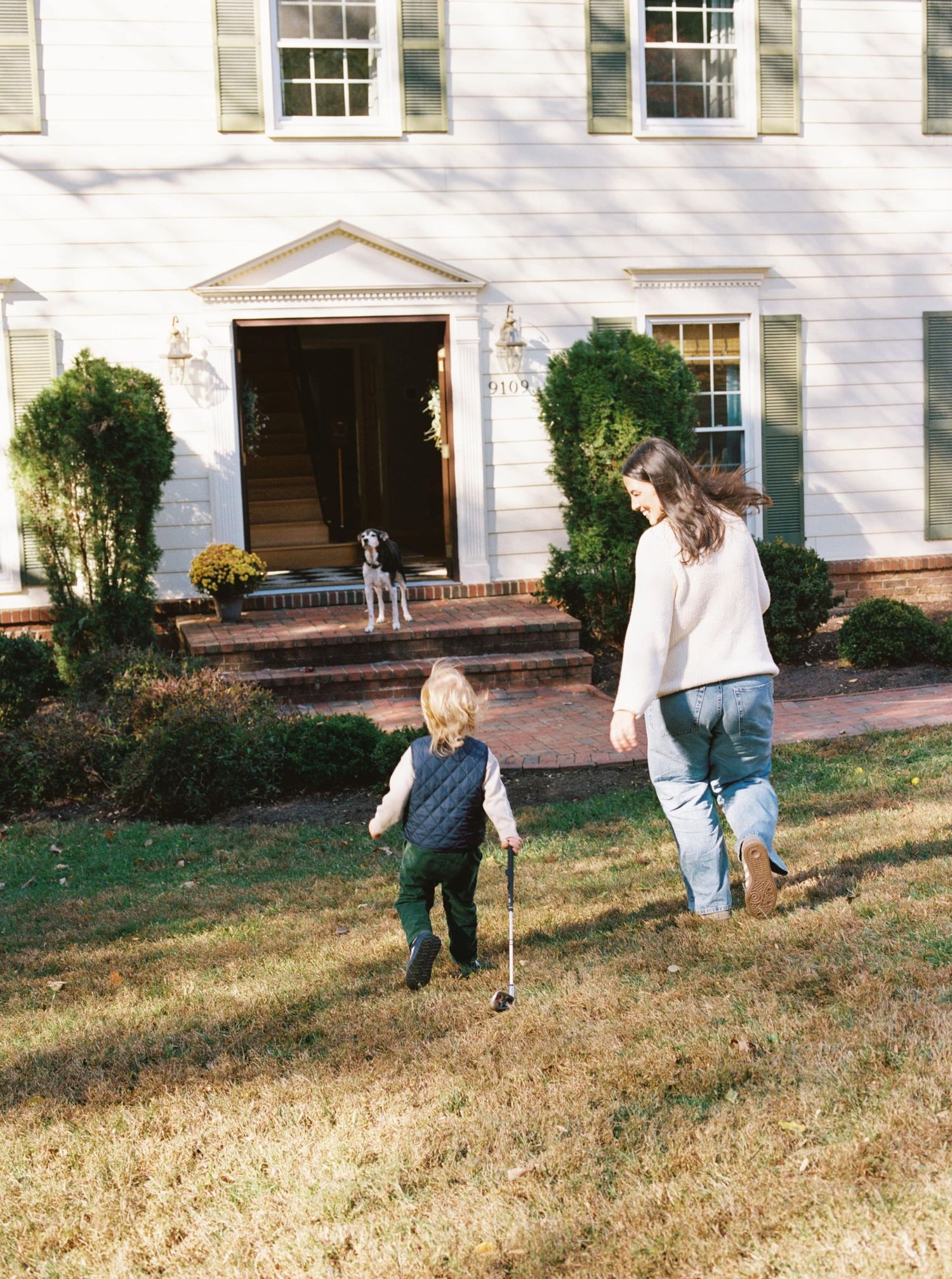 Two people walk across a sloped lawn in front of a white colonial style building with windows and columns.