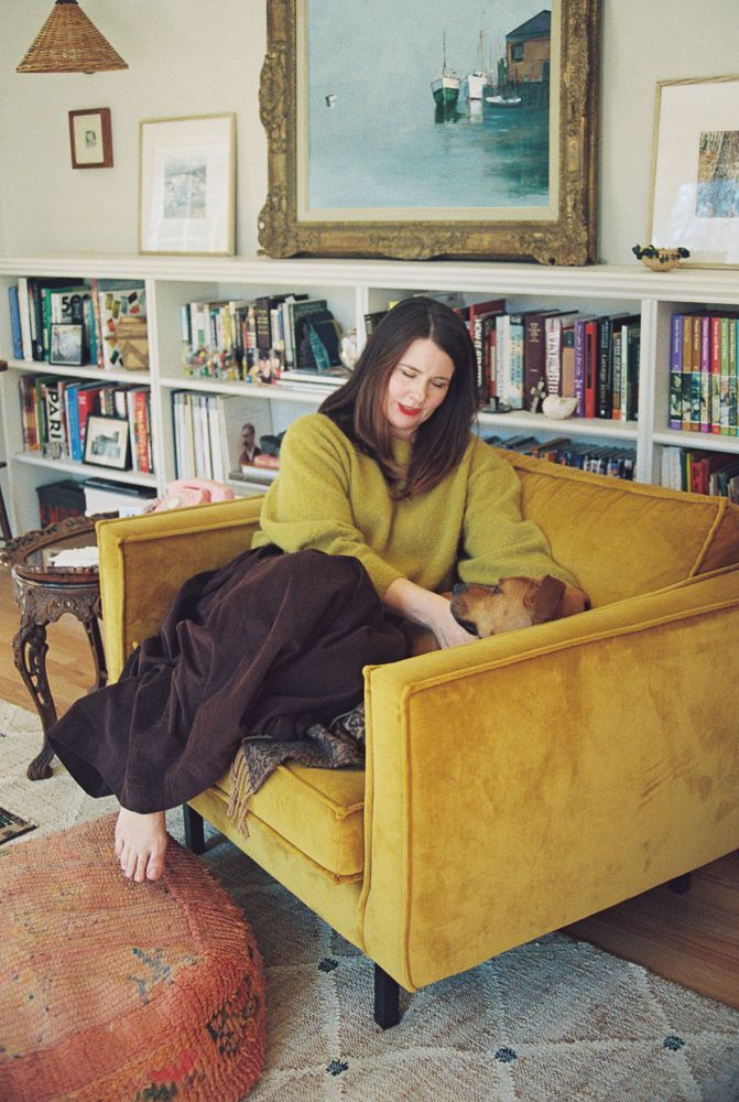 A series of four connected images showing someone lounging on a mustard yellow velvet couch with bookshelves in the background.