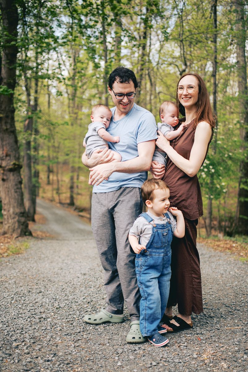Happy family with twins and toddler posing on a forest path in spring.