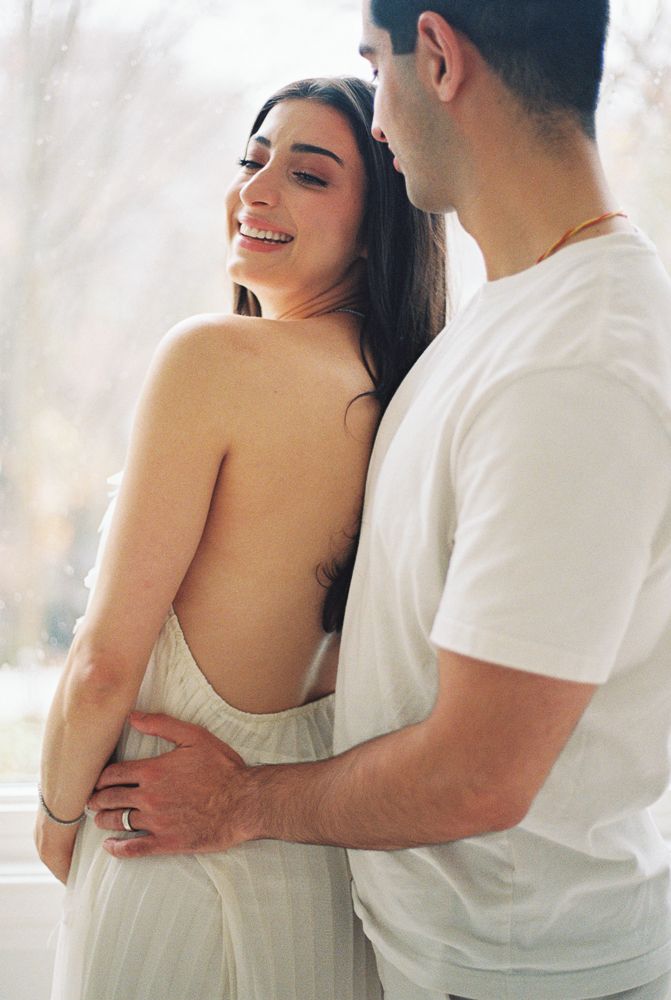 A couple in white outfits share intimate moments in a bright indoor setting, showing affection and laughter.