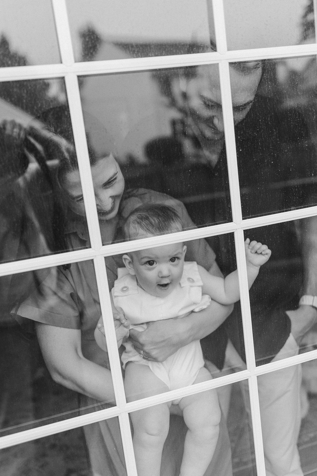 Black and white photo showing young children peering through a glass window with playful expressions.