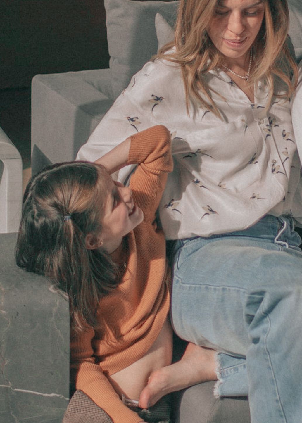 Person in orange shirt and jeans lying on white couch at home and resting with casual pose in natural lighting.