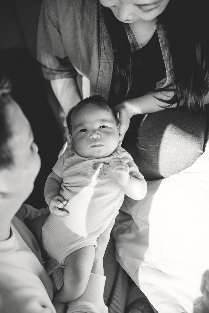 Black and white photo of a newborn baby being held by parents, looking up with tiny hands raised.
