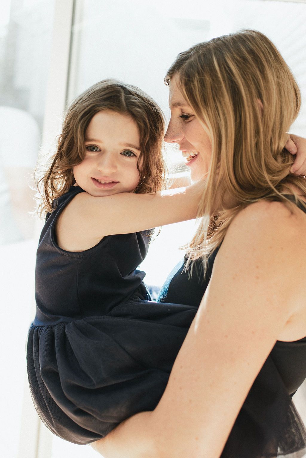 Series of tender moments between parent and child in black sweater against bright window light.