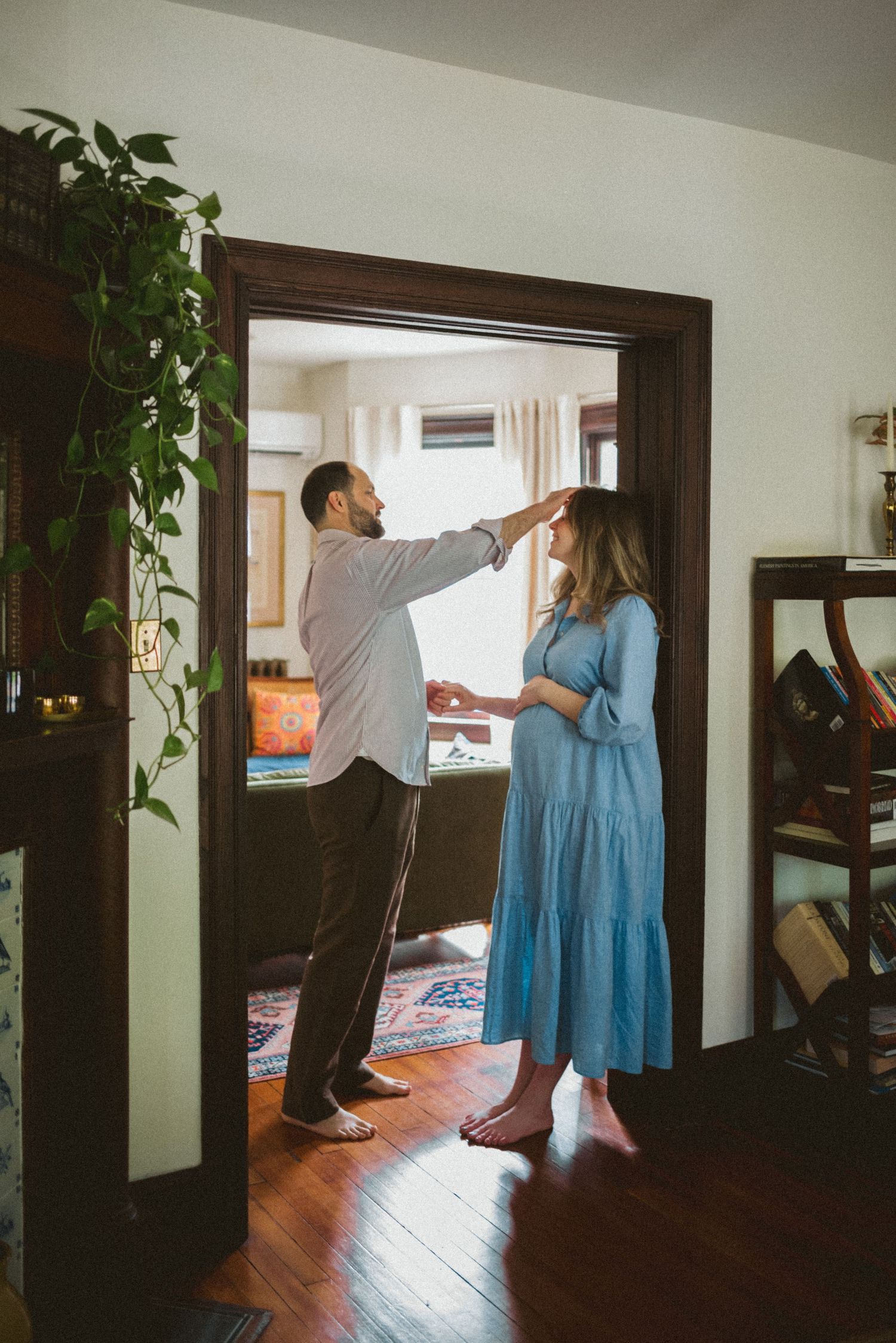 Two people share a playful moment in a doorway of a home with hardwood floors and a trailing houseplant.