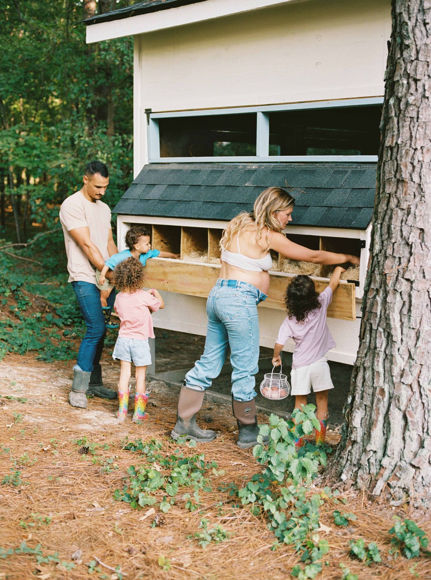 A family explores a rustic wooden chicken coop together on a wooded property.