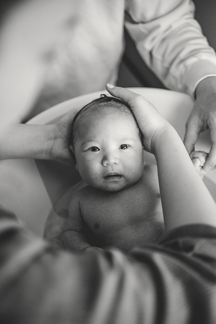 Black and white photo of a newborn baby being cradled in adult hands, looking up with wide eyes.