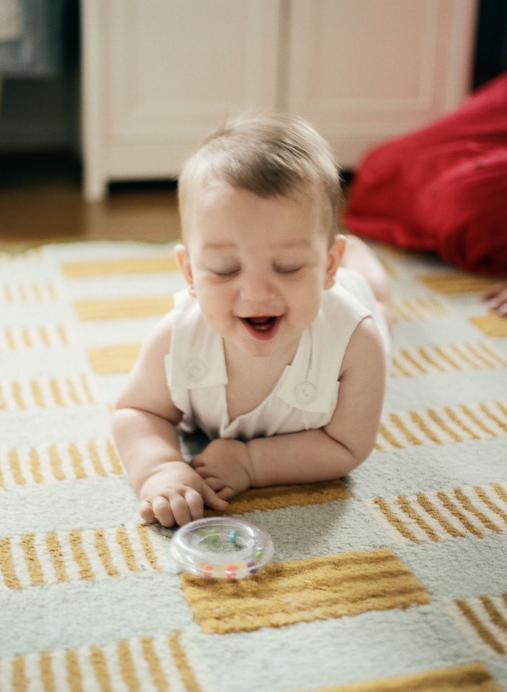 A baby lays on a striped carpet blowing bubbles through a tiny straw-like tool.
