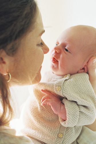 A mother tenderly holds her newborn baby, gazing lovingly at each other in a warm, softly lit setting.