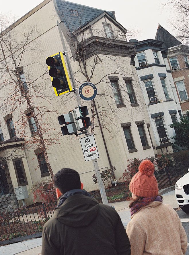 People walking past historic buildings on a winter day with traffic lights and bare trees visible.
