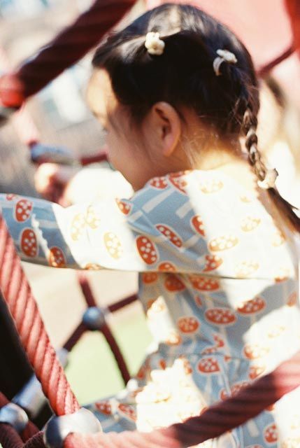 Back view of a young Asian girl with braids wearing a mushroom-print dress on a playground.