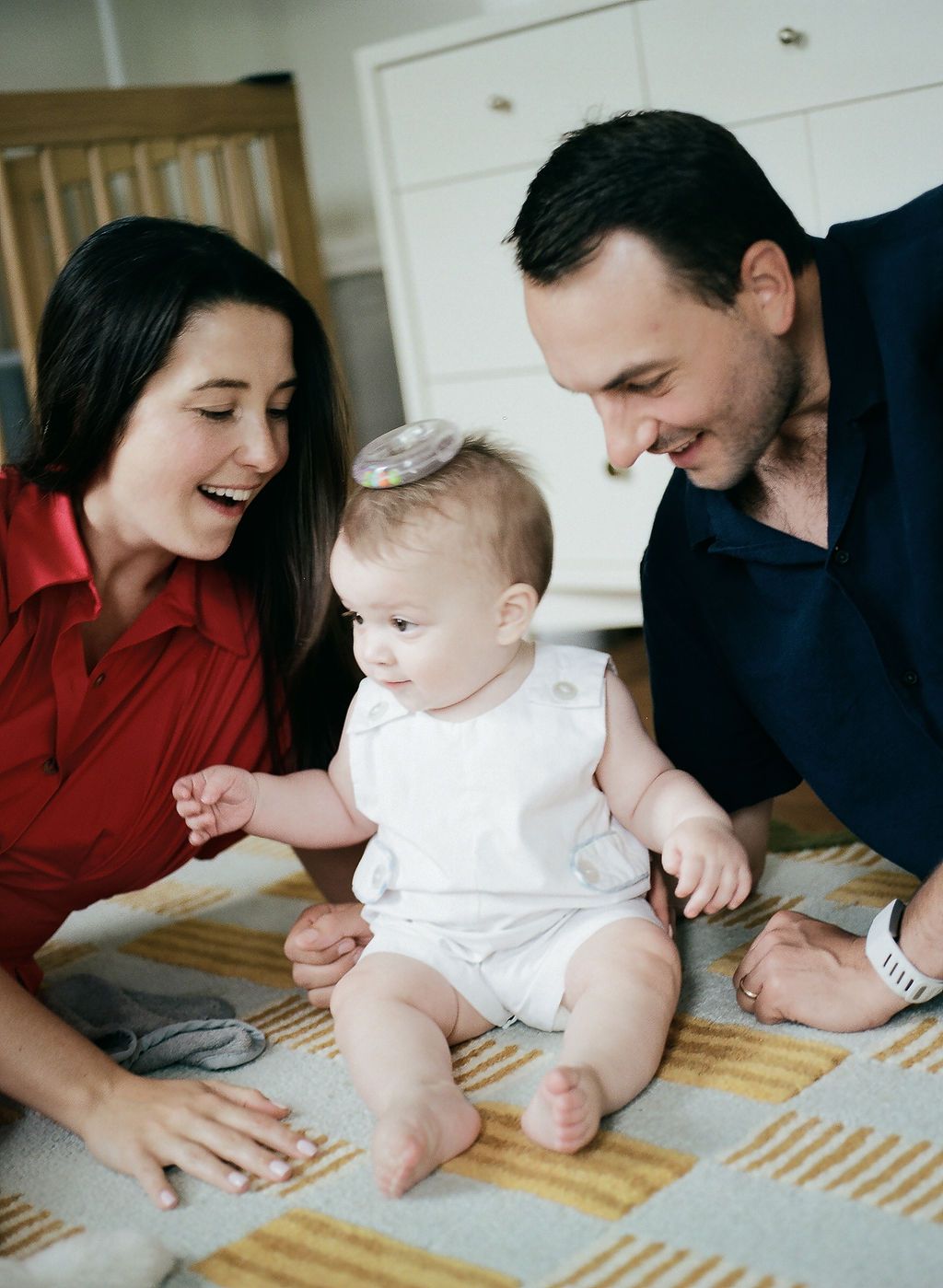 A playful intimate family moment captures adults gathered around an infant laying on a patterned blanket.