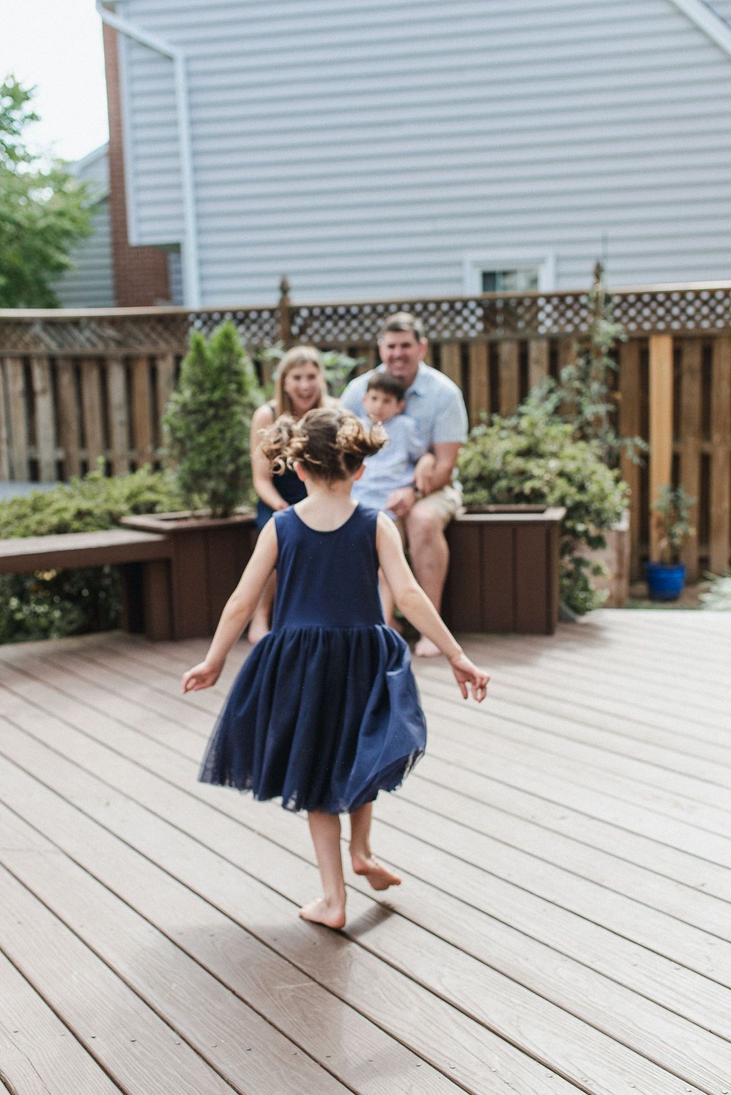 Two young children in matching navy blue dresses twirl and dance together on a wooden deck on a sunny day.