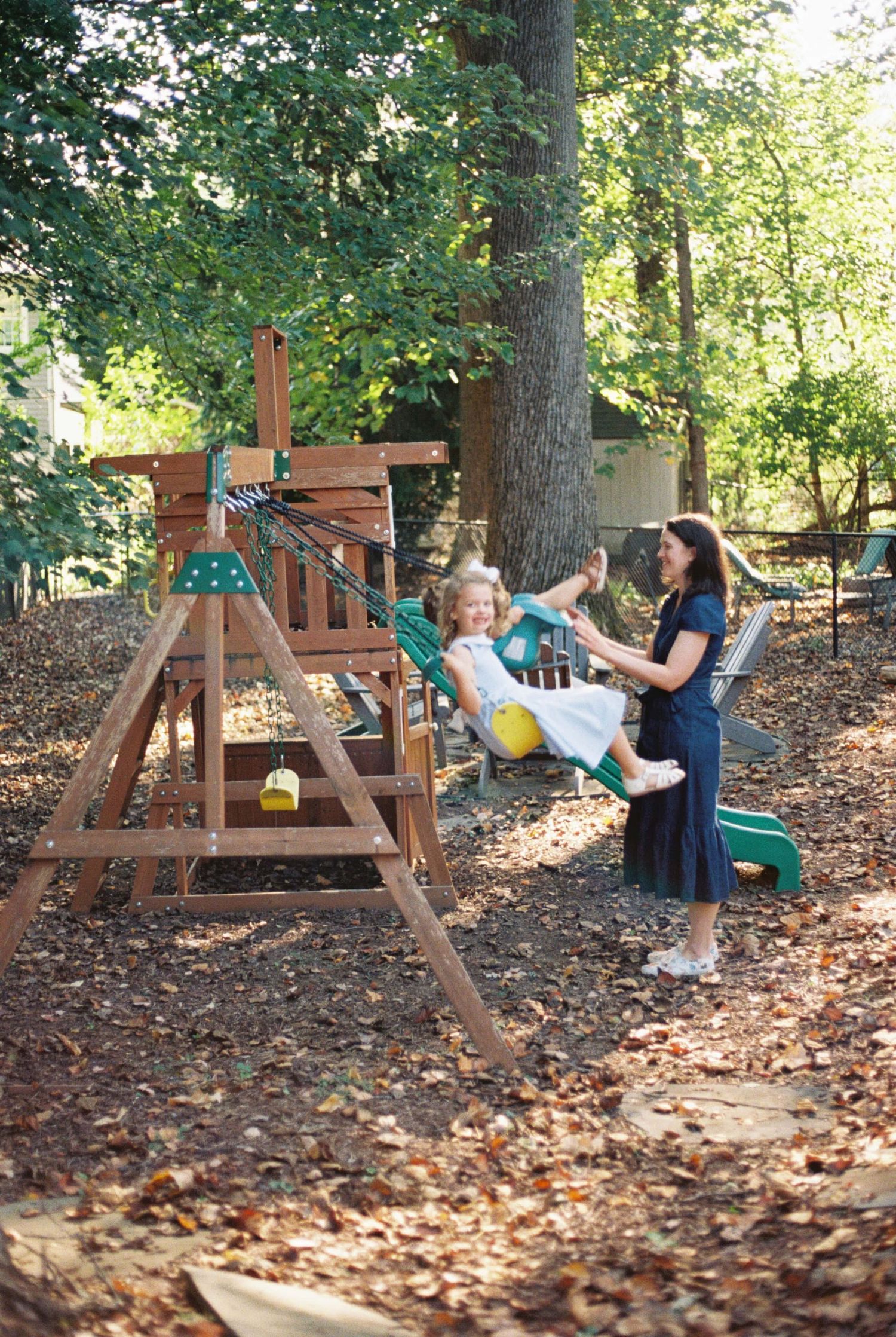 Children enjoying playtime on wooden swing sets in a backyard playground covered with autumn leaves.