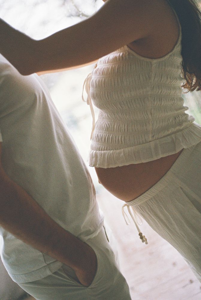 Ethereal white fabric drapes over a pregnant figure in soft natural light.