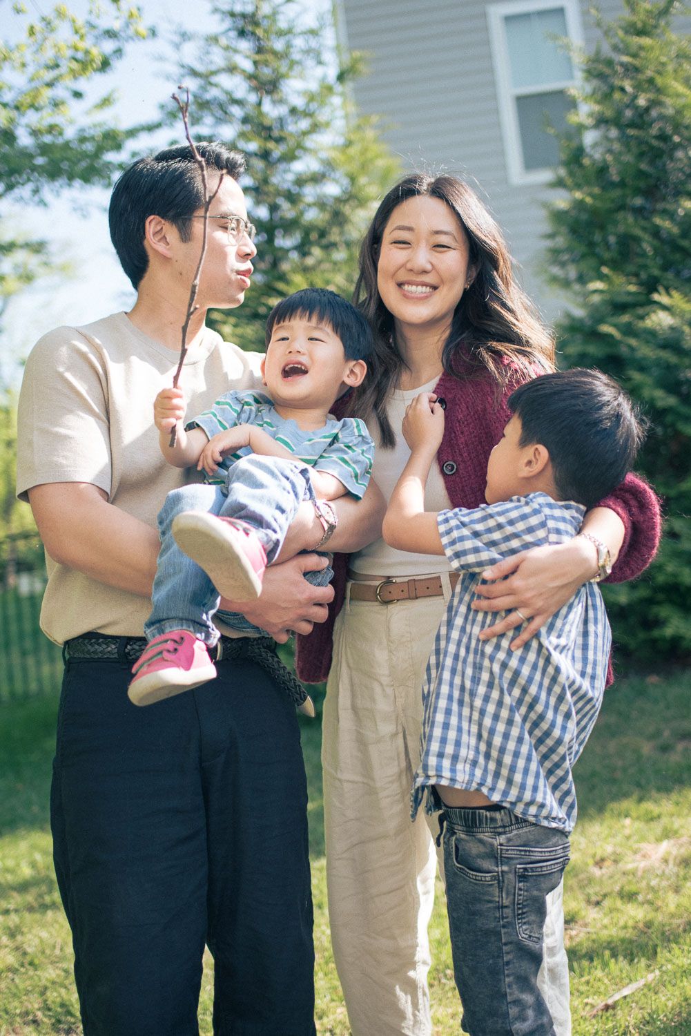 Happy Asian family with two young children laughing and playing together outdoors in a green backyard.