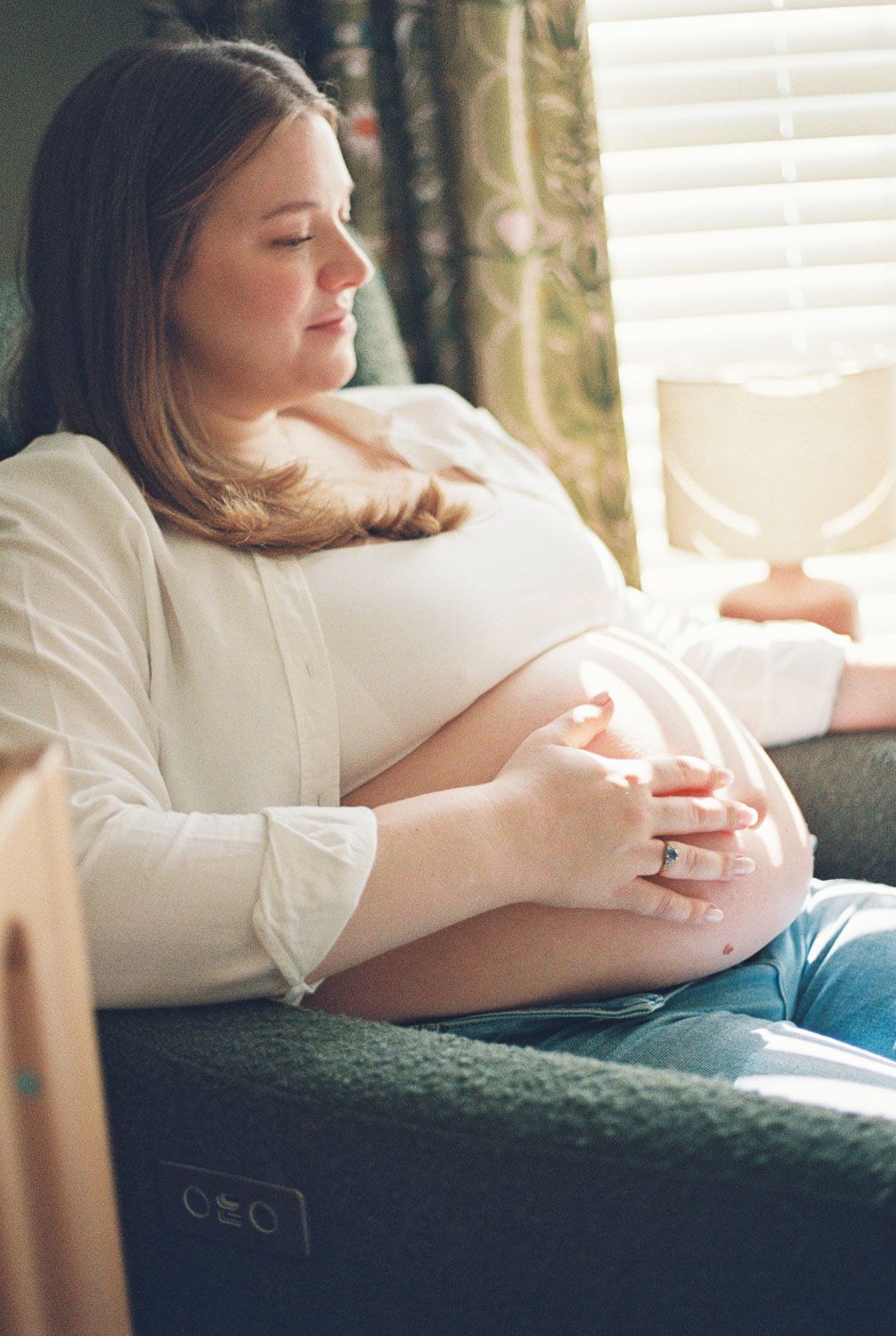 Pregnant woman sitting on sofa cradling her baby bump in soft natural window light.