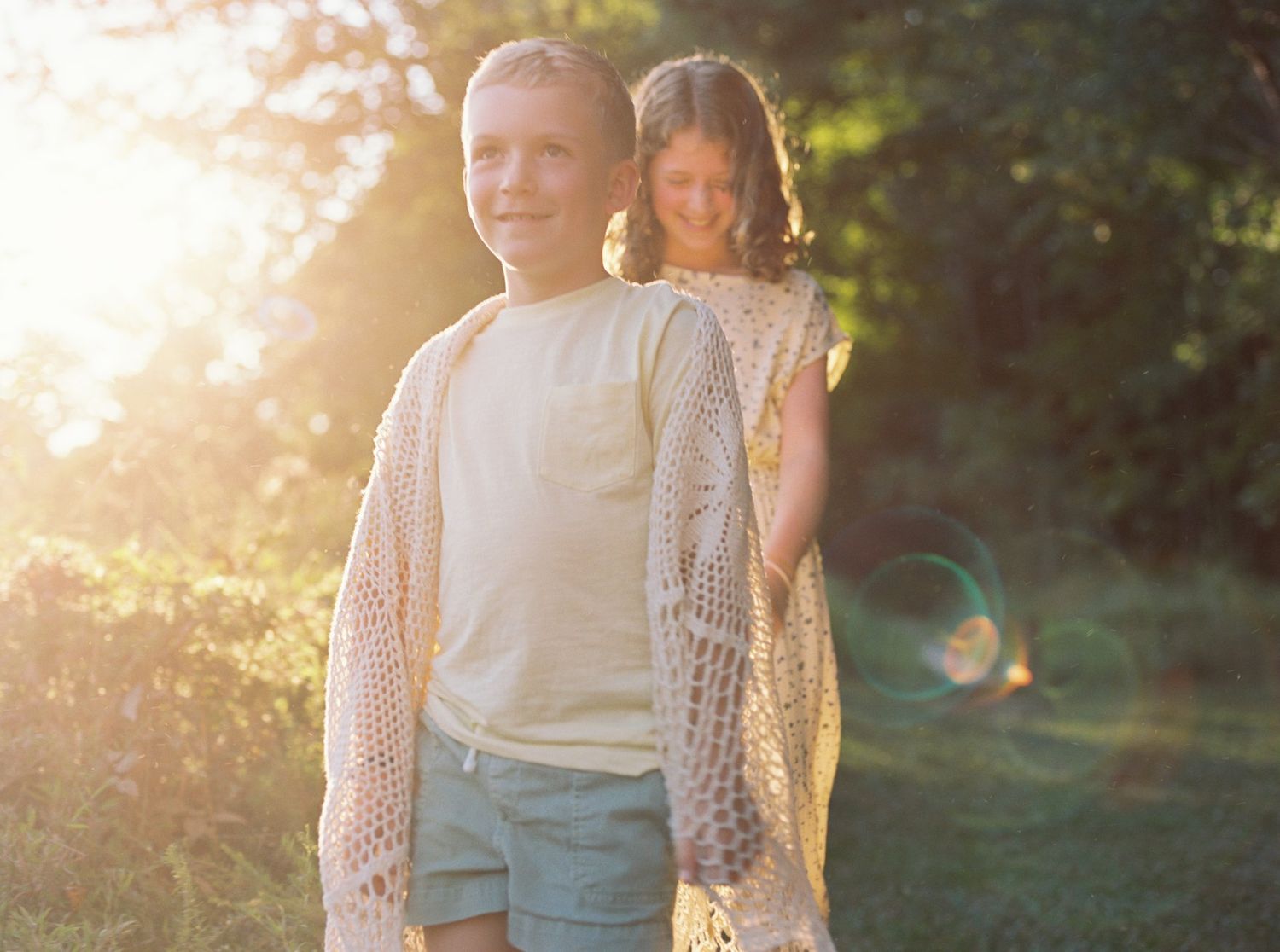 A couple walks hand in hand through a sunlit garden path during golden hour.