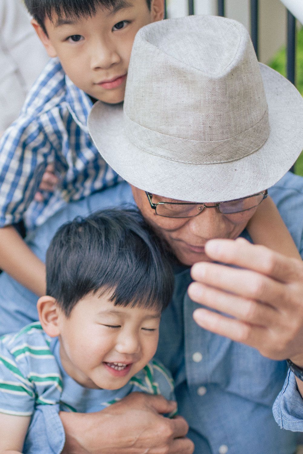 Grandfather in hat sharing joyful moment with two young Asian grandsons on porch steps.