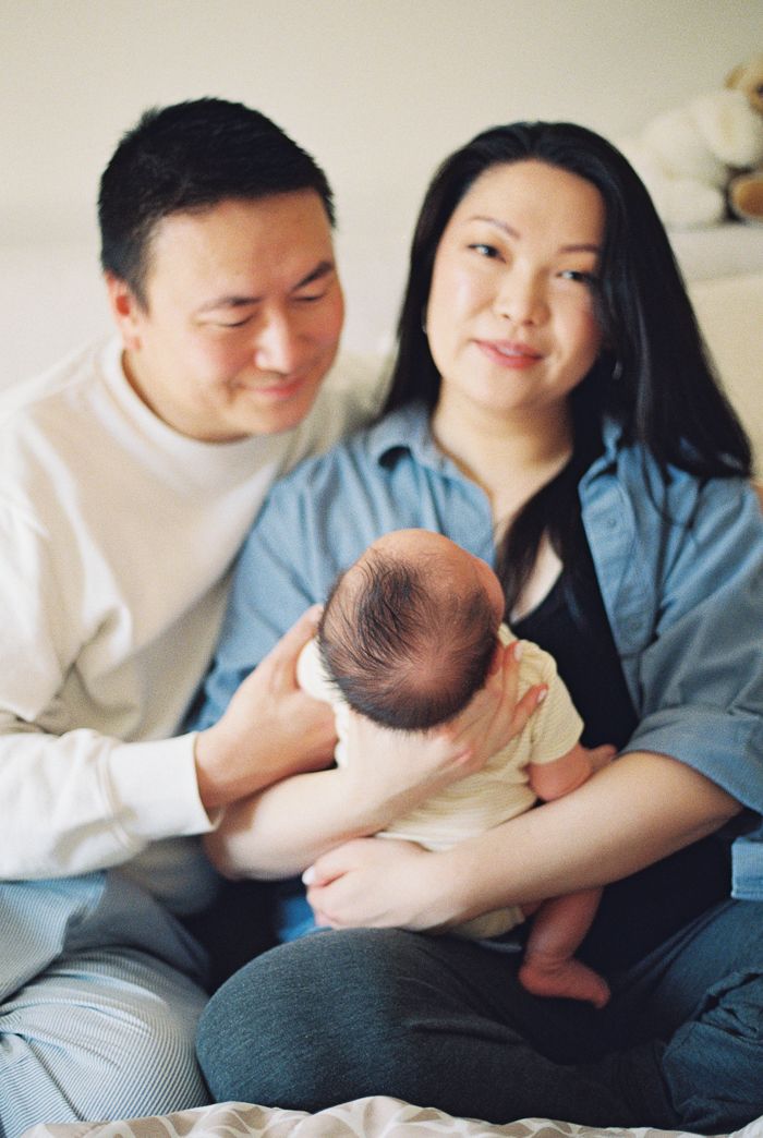 Happy Asian family portrait with parents smiling and cradling their newborn baby at home.