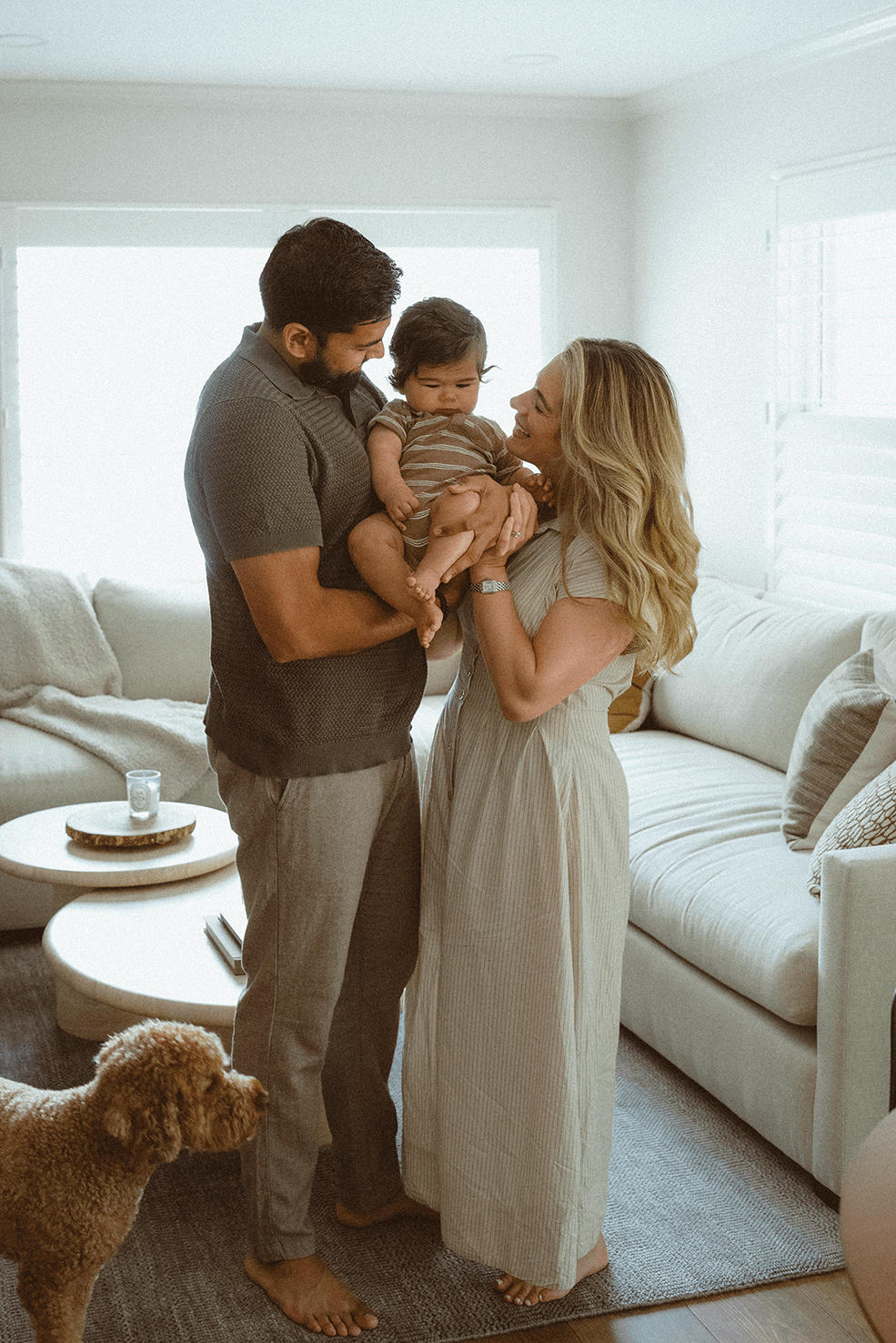 A family shares intimate moments together in their bright living room with a brown dog beside their white couch.