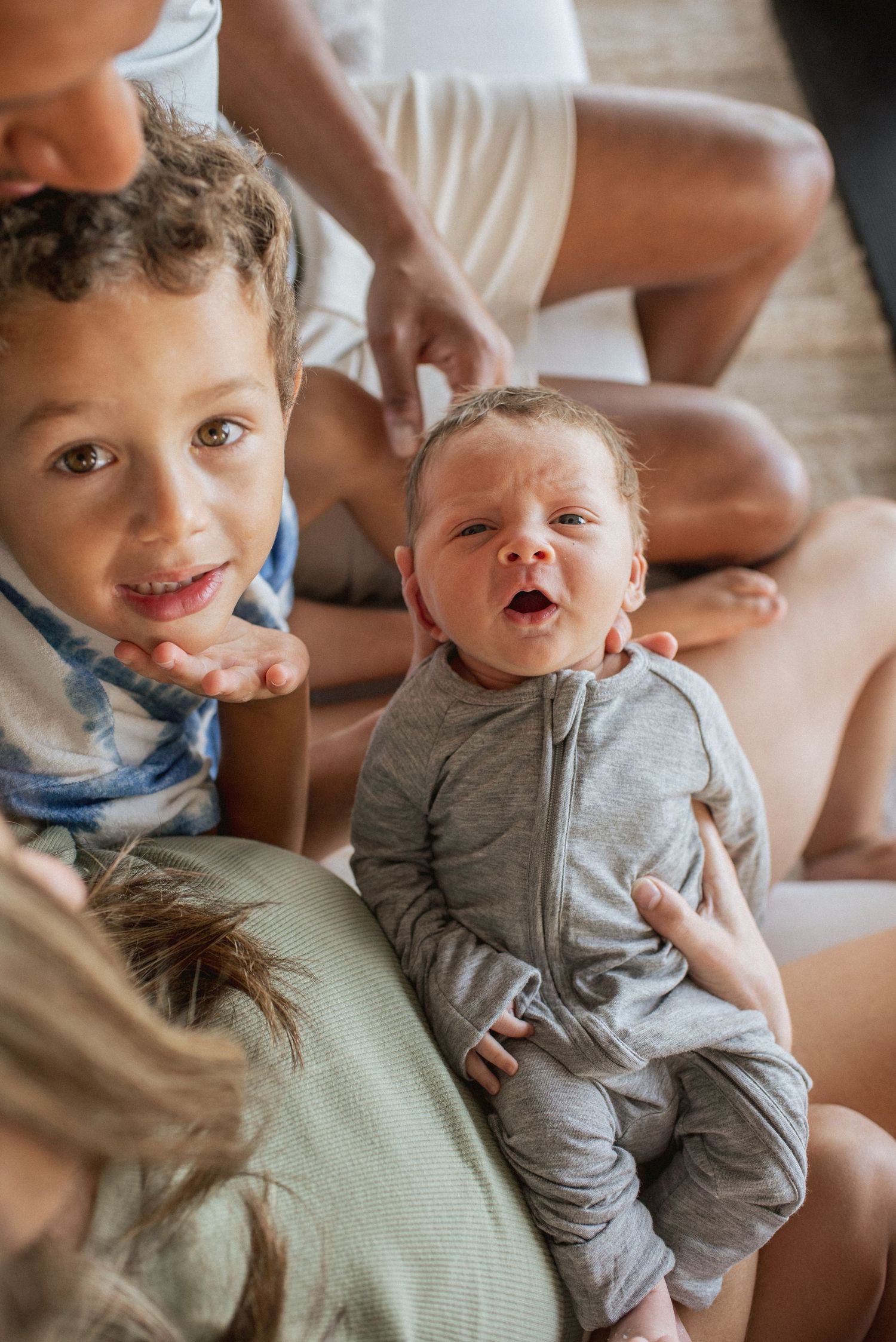 Two children playfully interact and laugh while wearing casual clothes in natural indoor lighting.