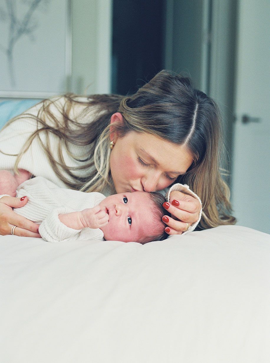 Parent and newborn baby share tender moment of bonding while resting together on white bedding.