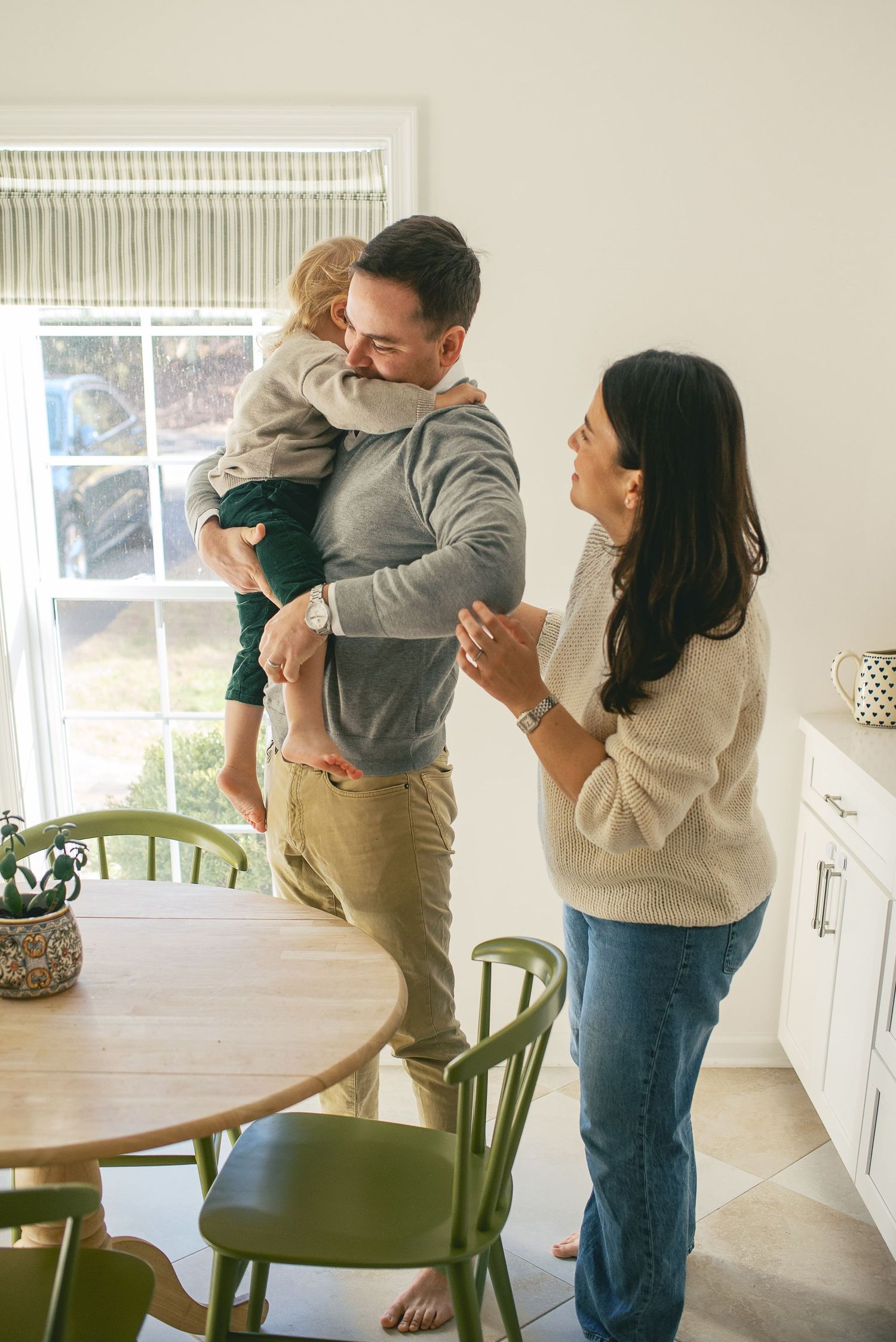 A family shares a joyful moment together in their bright kitchen with green chairs and a wooden dining table.