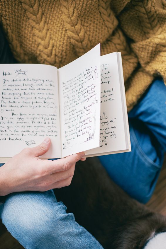 A hand holds an open handwritten journal against a backdrop of cozy knit sweater and blue denim.