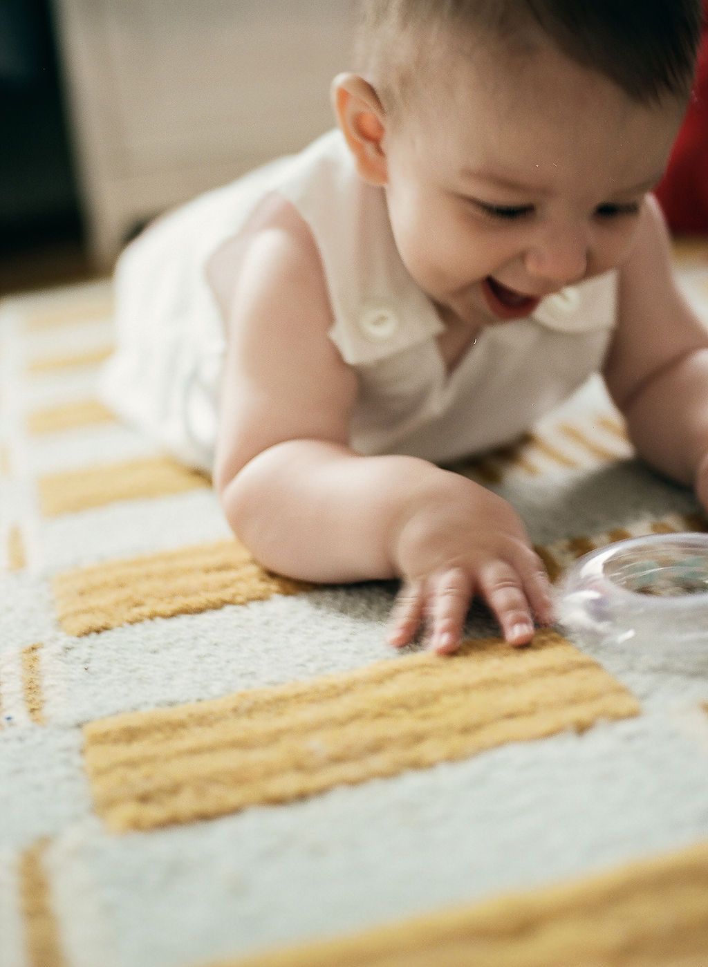 Baby in white clothing explores and crawls on a textured beige surface.