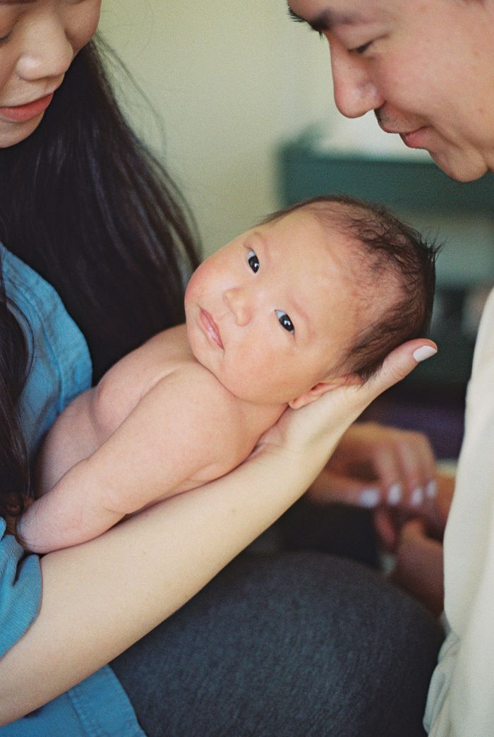 Newborn baby with dark hair being cradled in parents arms, looking up alertly at mother and father.