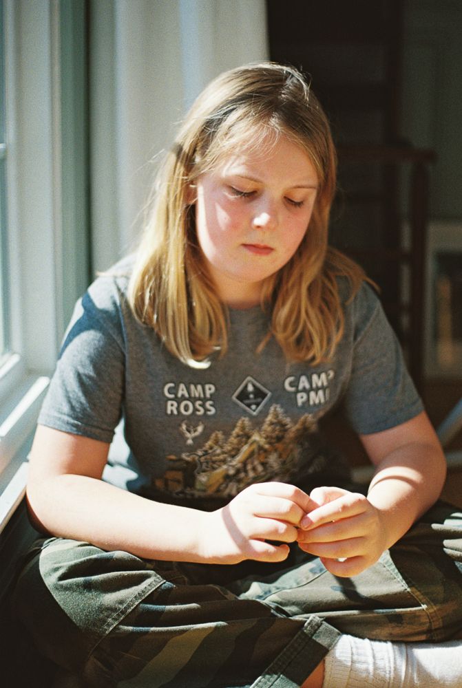 Person in gray t-shirt carefully works on a detailed craft project in natural window lighting.