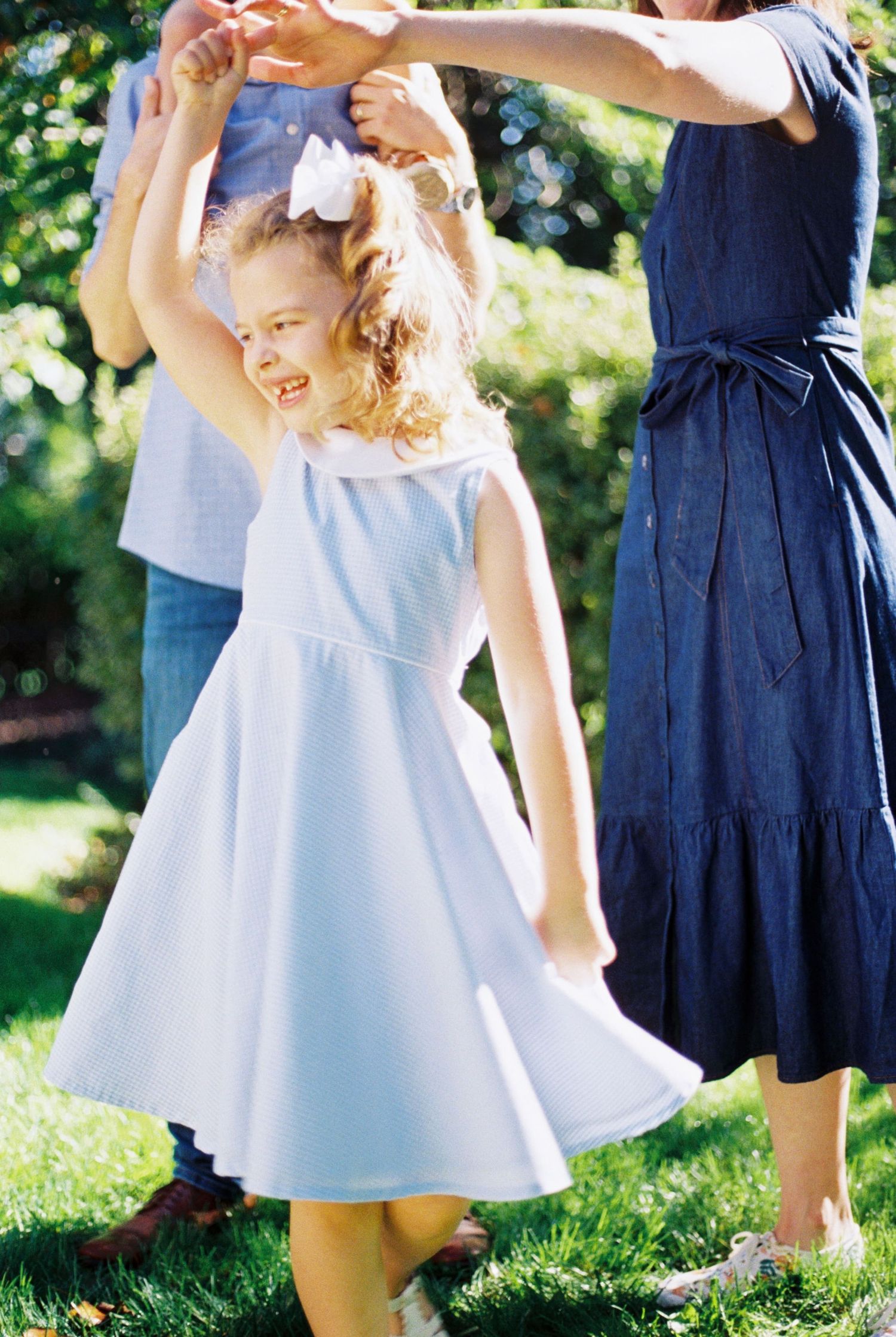 Two people in white and navy dresses dance together in a sunny garden setting with natural lighting and greenery.