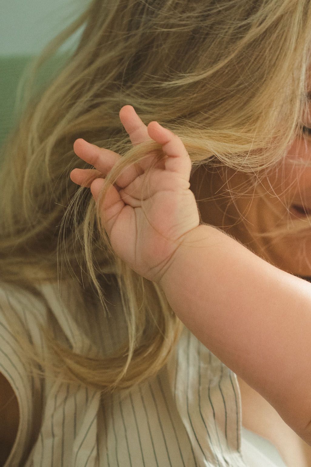 A small child's hand reaches up while playing with long blonde hair in soft lighting.