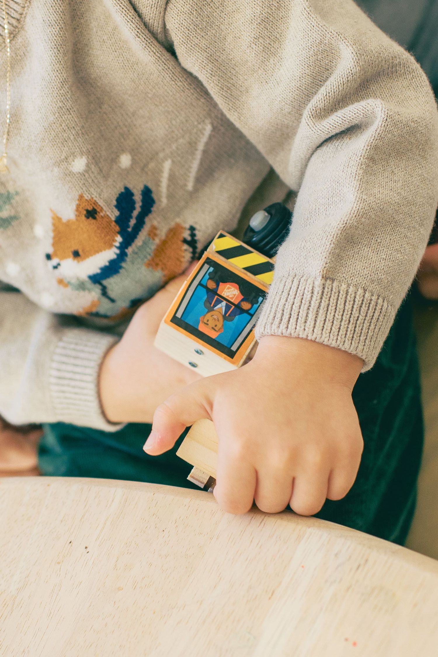 Close-up view of hands wearing a light gray sweater with colorful embroidered details on the sleeve.