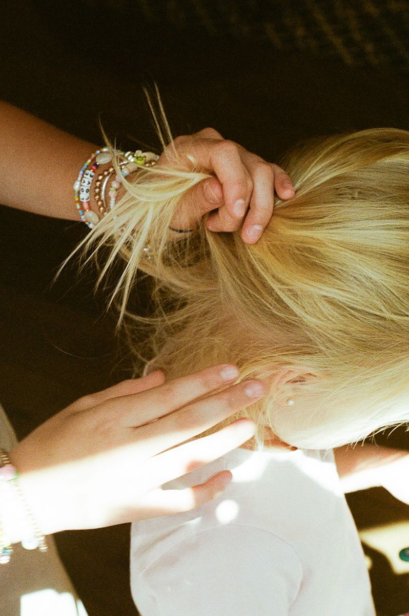 Hands with bracelets styling blonde hair in natural lighting.