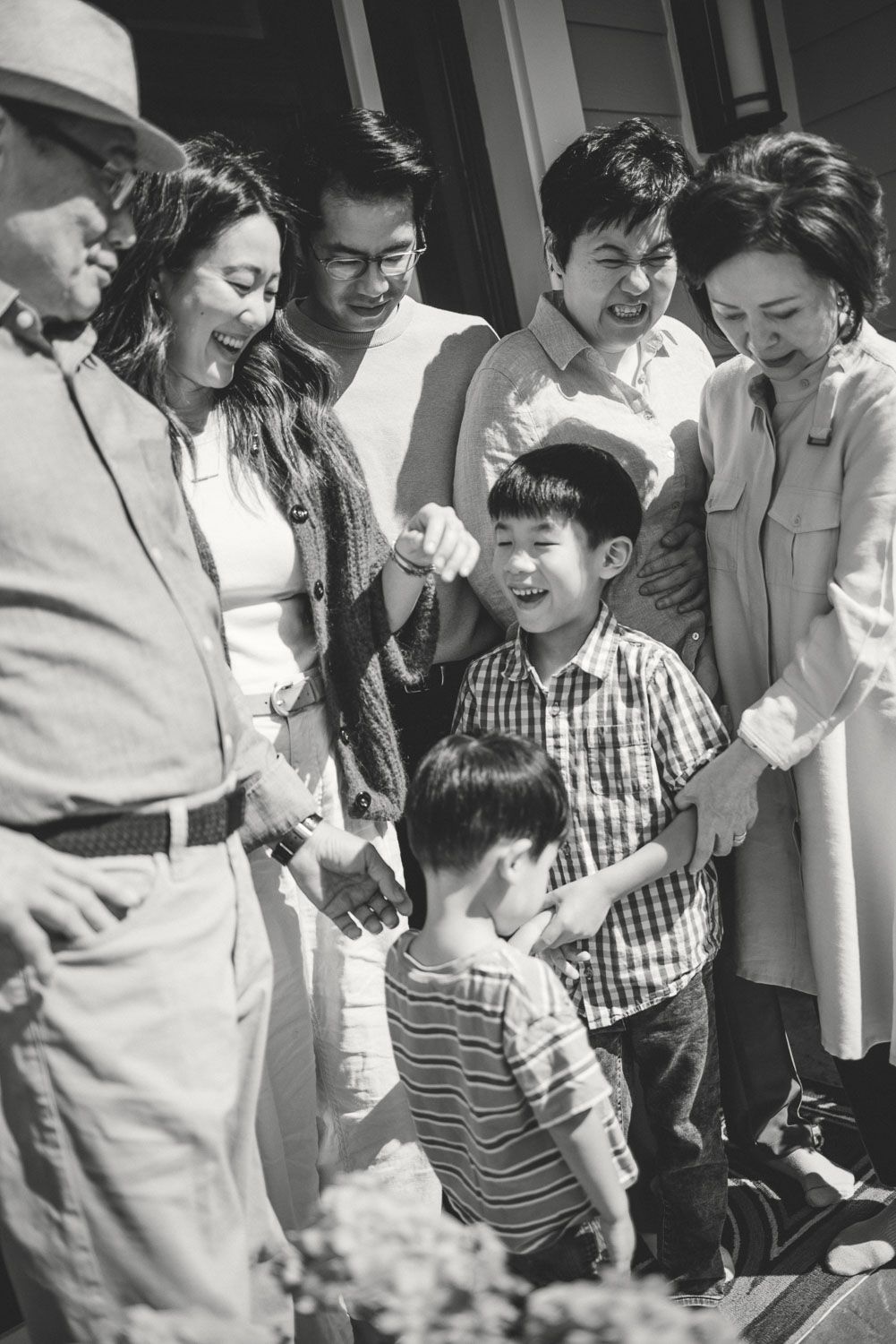 Black and white photo of a multigenerational Asian family gathering outdoors, with children and adults smiling together.