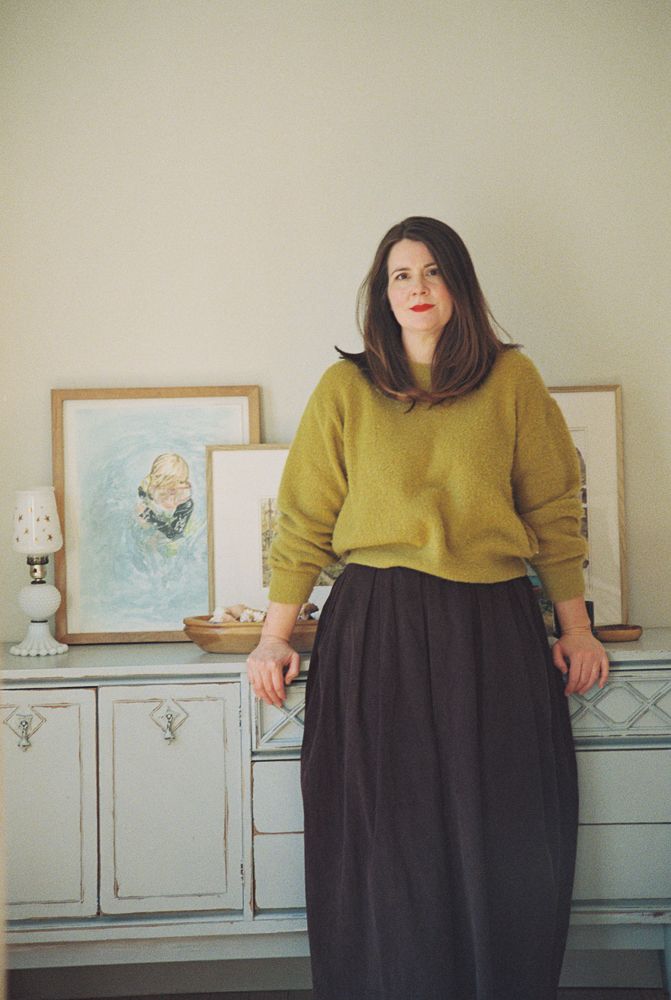 A series of five photos showing someone in a mustard yellow sweater and black skirt standing against a light colored wall.