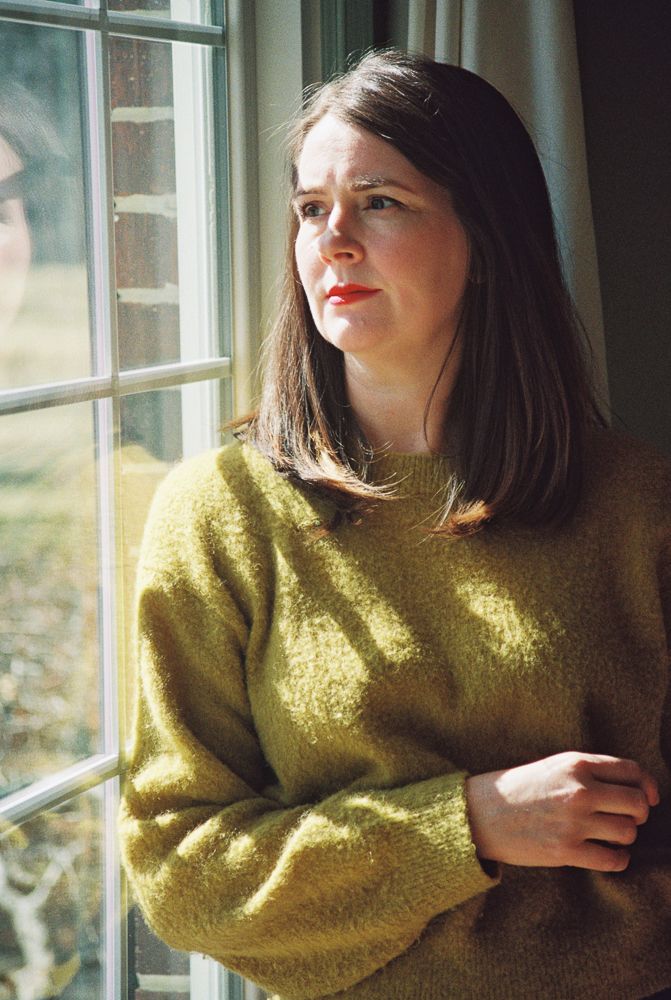 A person in a mustard yellow sweater gazes thoughtfully out of a sunlit window in a series of candid poses.