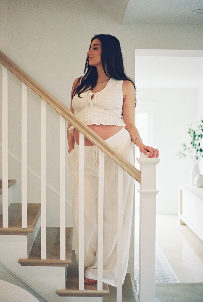 Woman in white dress descends elegant staircase with wooden handrail in bright modern interior.