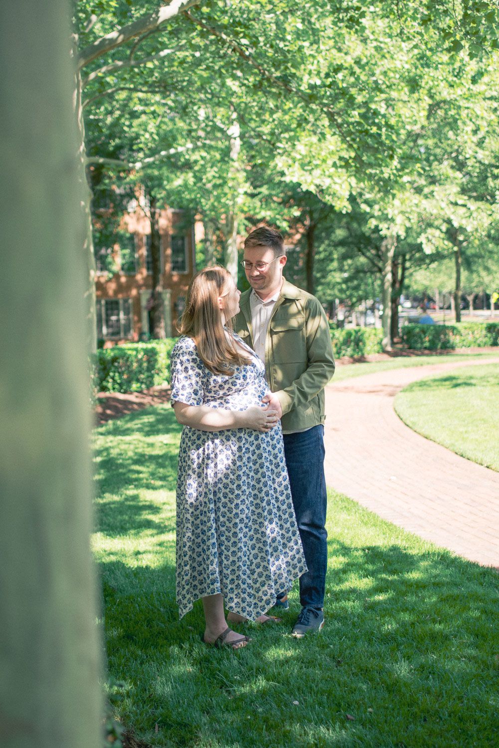 Expecting couple standing in a lush green park, man in green shirt tenderly touching pregnant woman's belly.