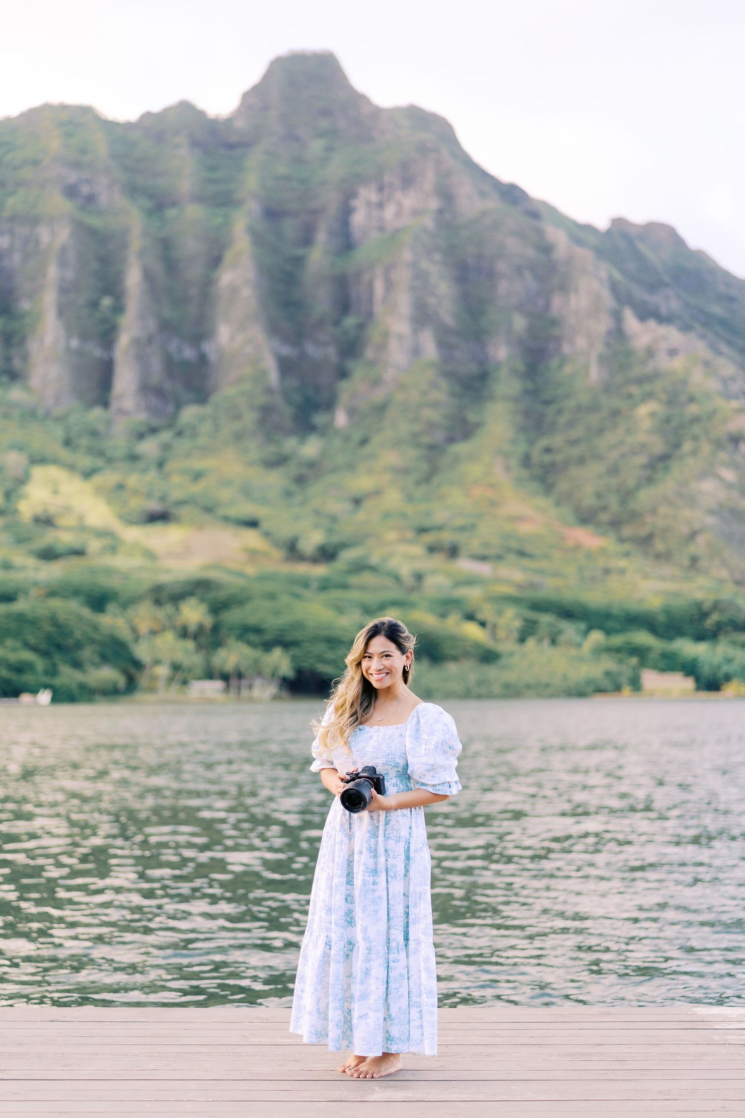 A photographer captures scenic shots at Kualoa Beach Park in Hawaii with dramatic mountain cliffs in the background.