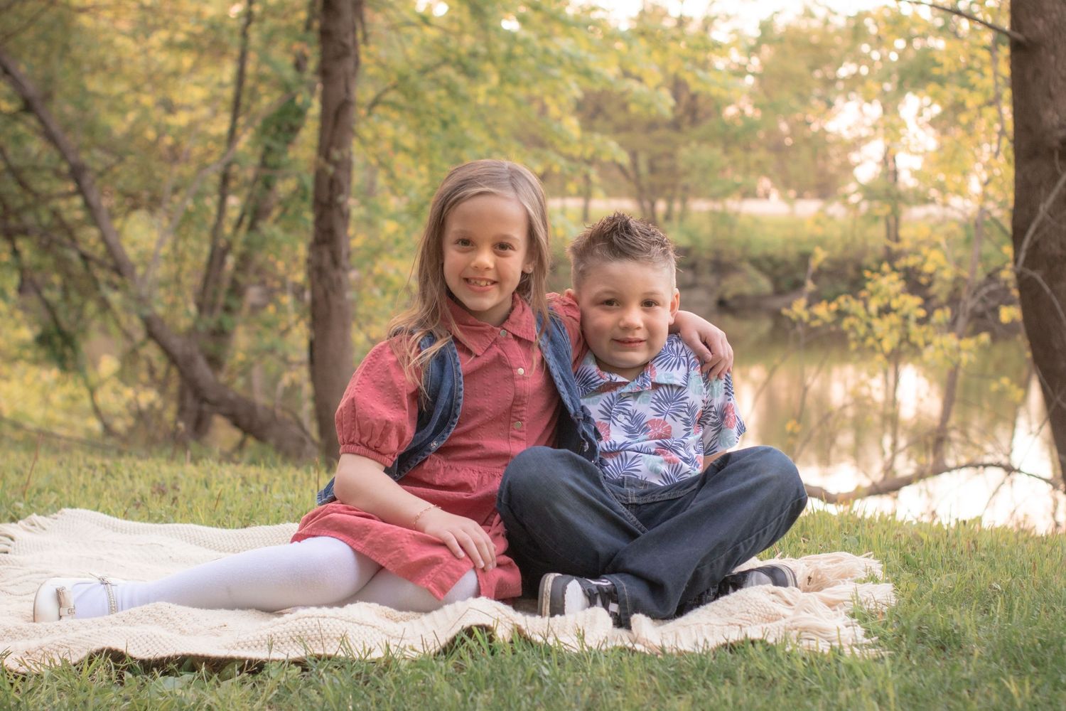 Brother and sister snuggled together on a blanket beside a pond during an outdoor family session in Indiana