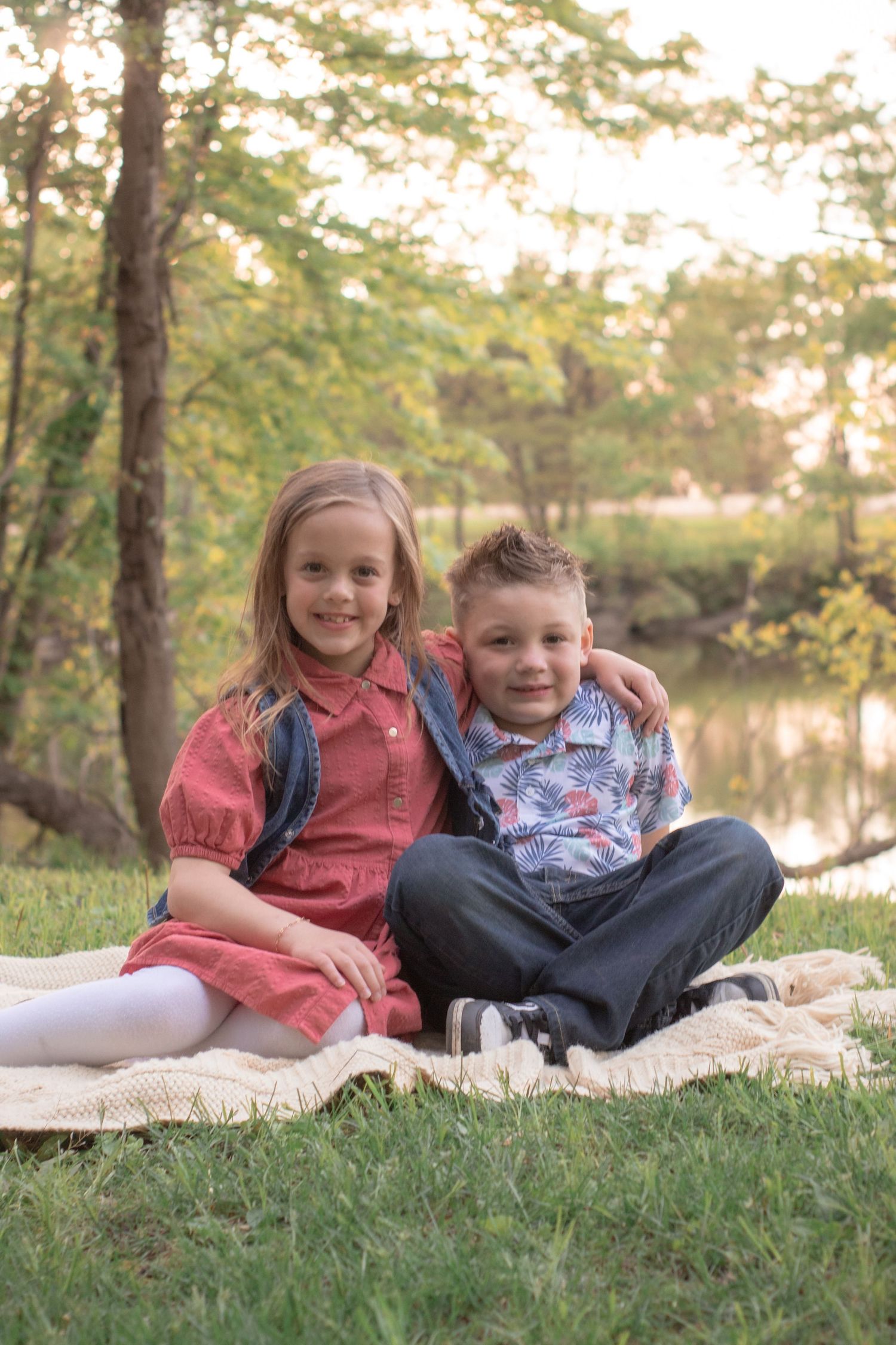 Brother and sister snuggled together on a blanket beside a pond during an outdoor family session in Indiana