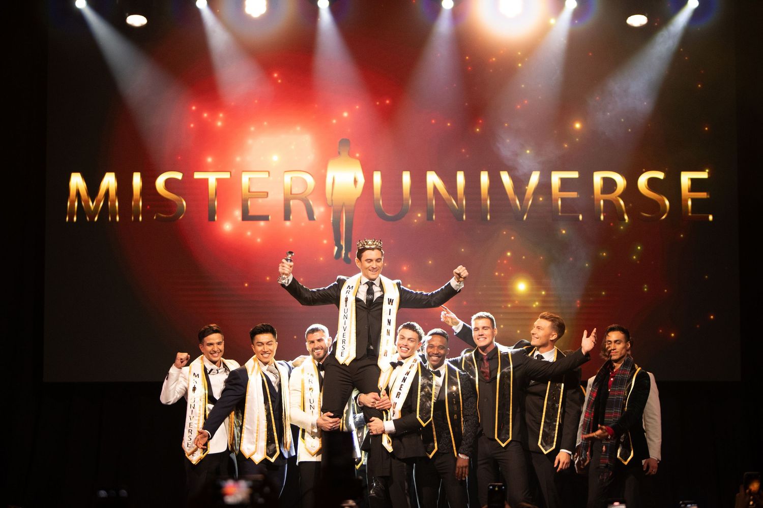 Stage performance with dramatic lighting and silhouetted performers at Mister Universe event.