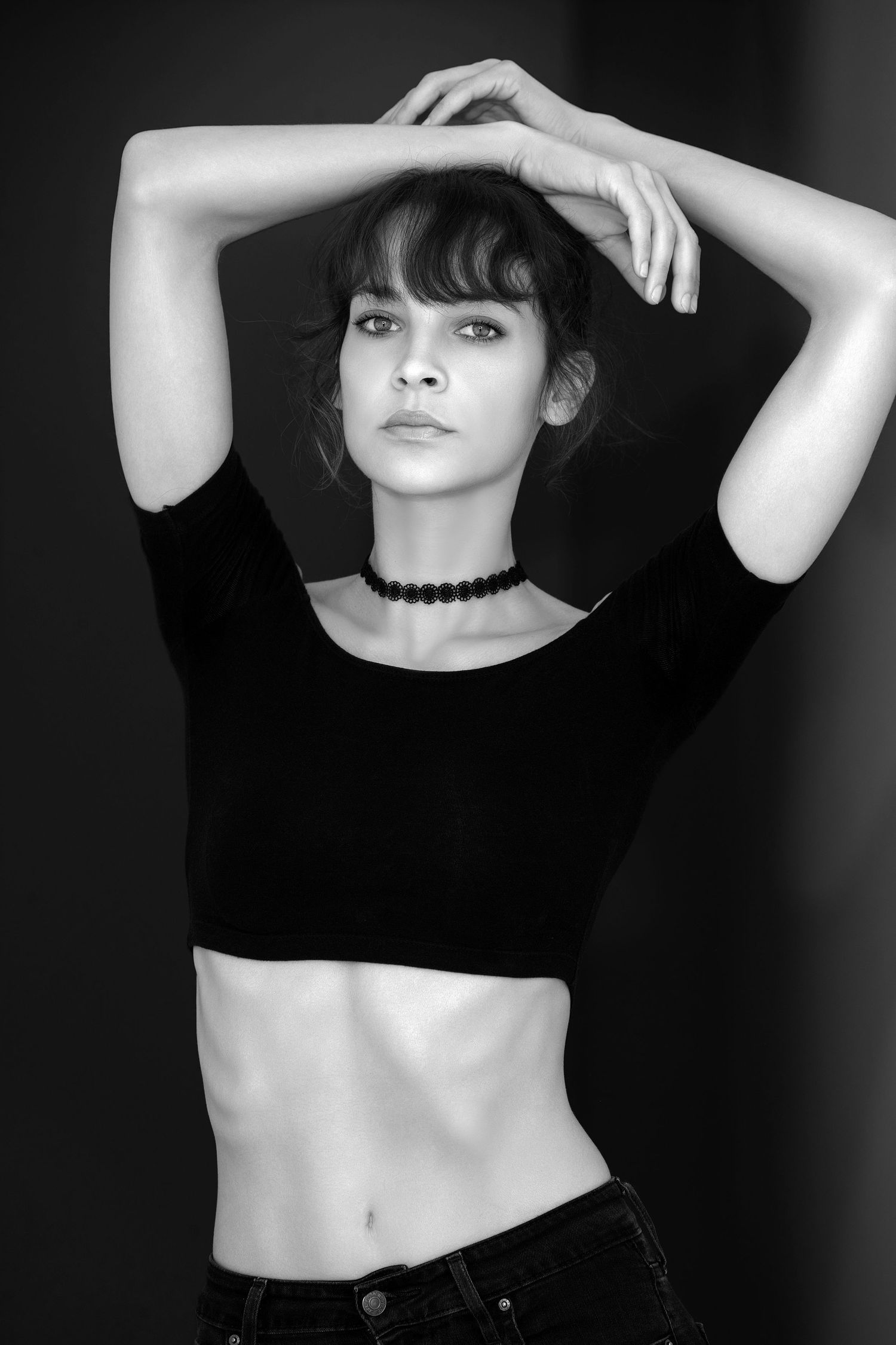 A dramatic black and white portrait series showing a figure in a black top posing with raised arms against a dark background.