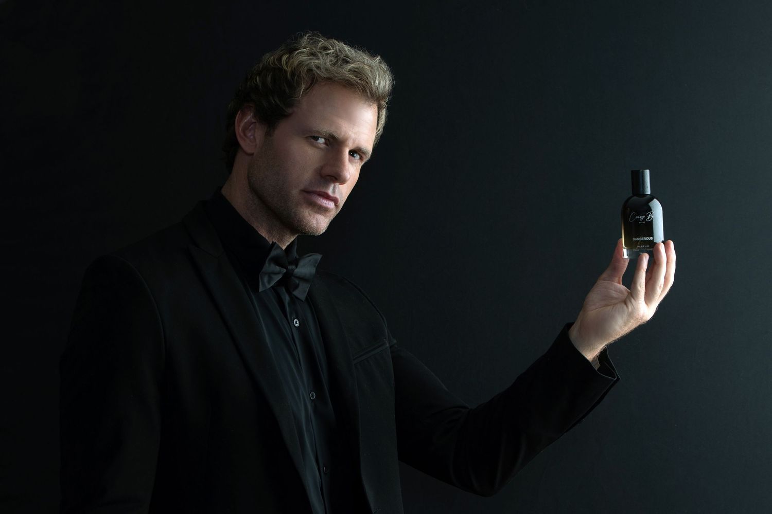 A person in a dark setting holds a mobile phone while looking away from the camera in a dramatic pose.